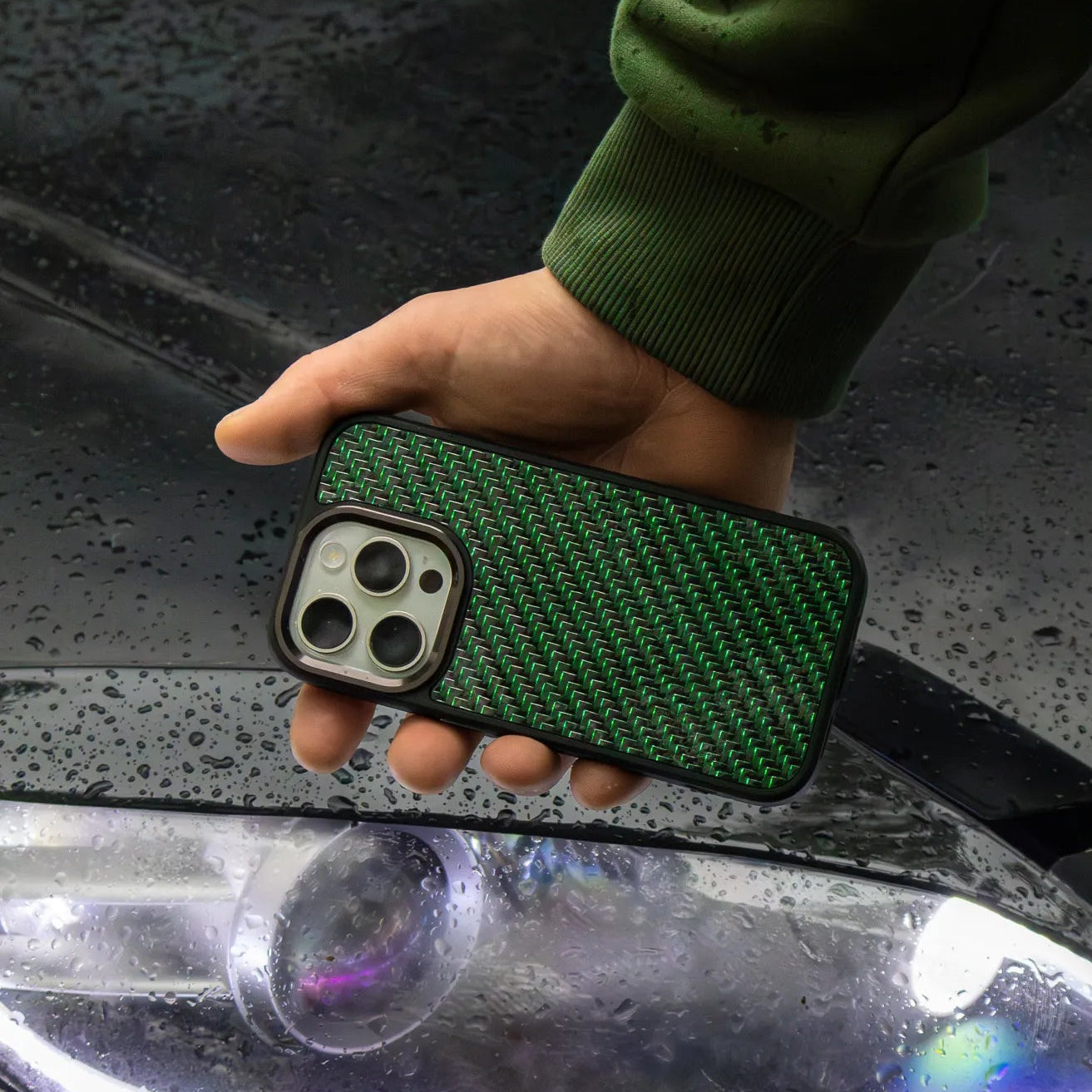 Person holding a green carbon fiber phone case with RX-8 headlight in the background