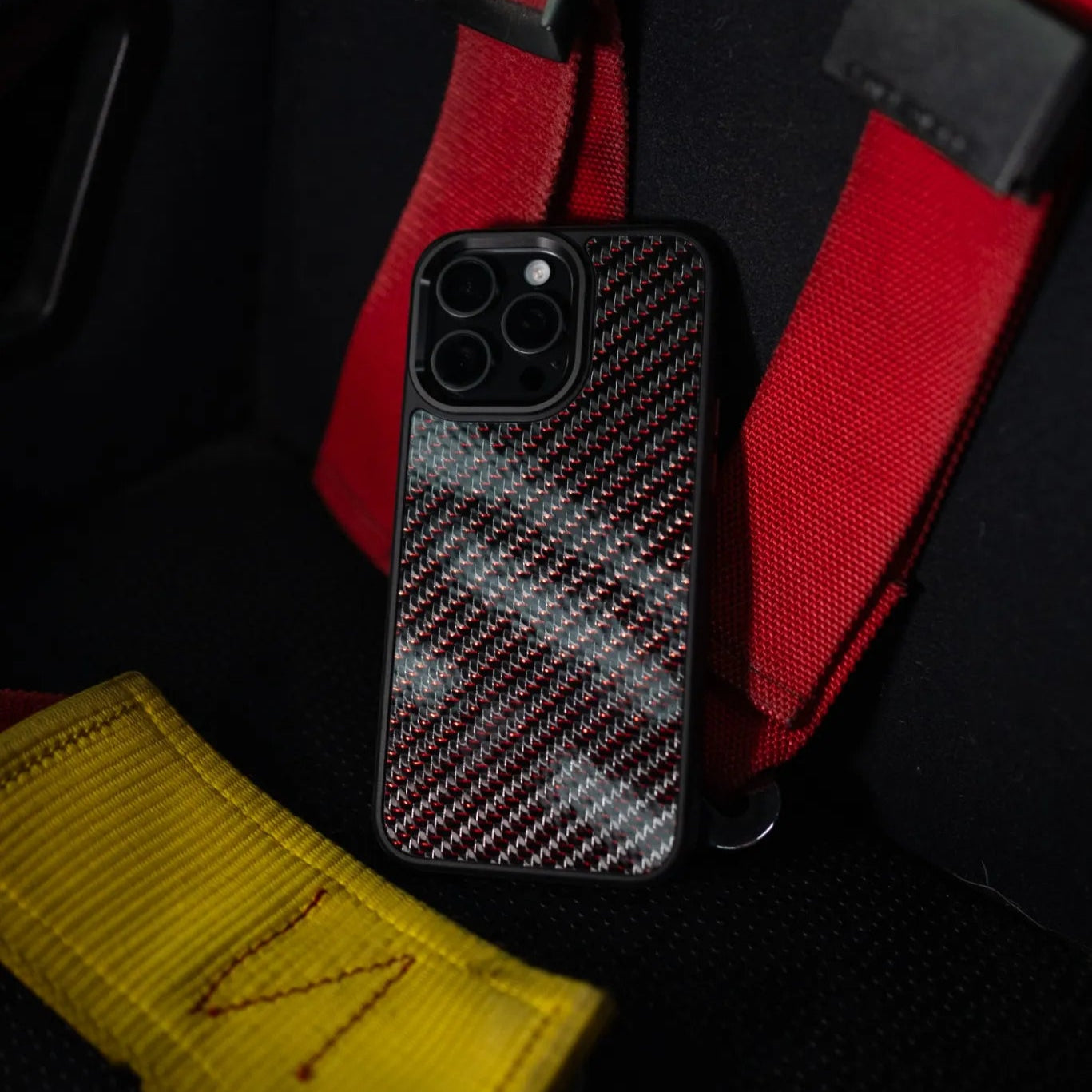 Phone case with carbon fiber on a red four point seatbelt

